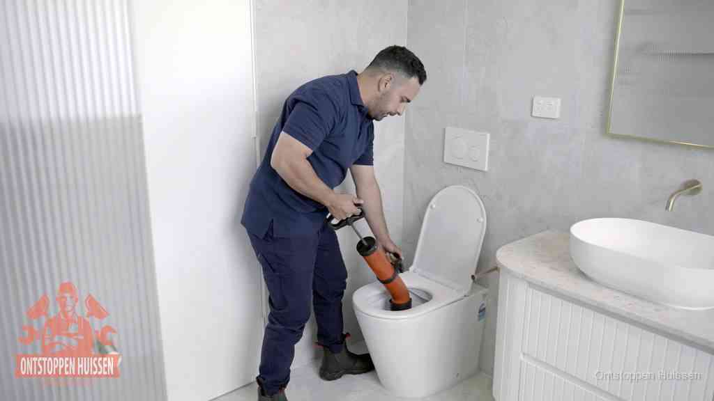 Een monteur buigt over een wandcloset en duwt met de hand een persluchtontstopper in de toiletpot om de verstopping handmatig los te maken in Huissen