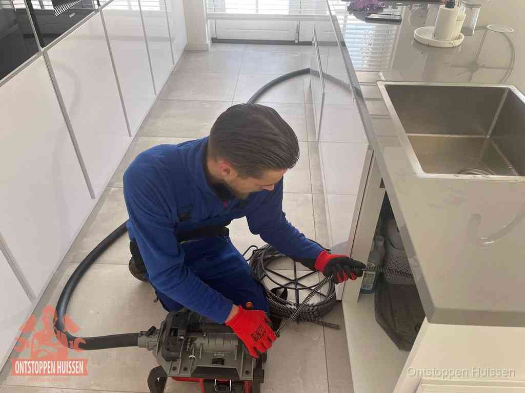 Een monteur ontstopt de keukenafvoer onder de spoelbak met een elektrische veermachine in Huissen