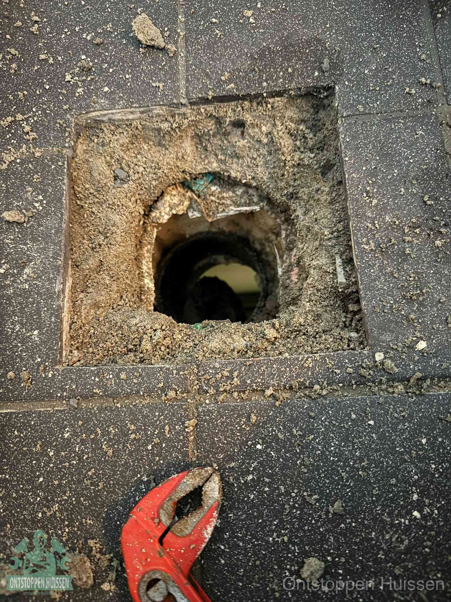 Een geopend rioolputje in een betontegelvloer met losgemaakt rooster en een zichtbare ronde afvoerbuis, het achterhalen waar de afvoerverstopping zit in Huissen