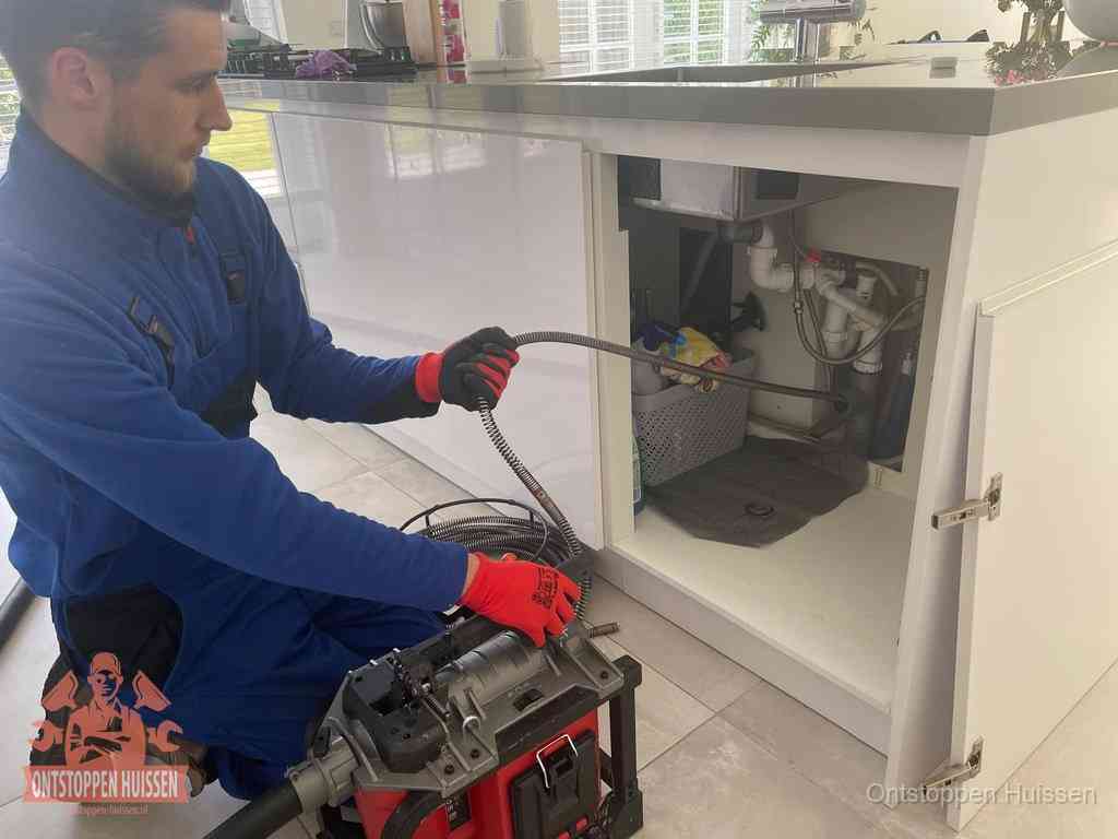 Monteur voert een ontstoppingsveer in de afvoer onder de keuken in Huissen