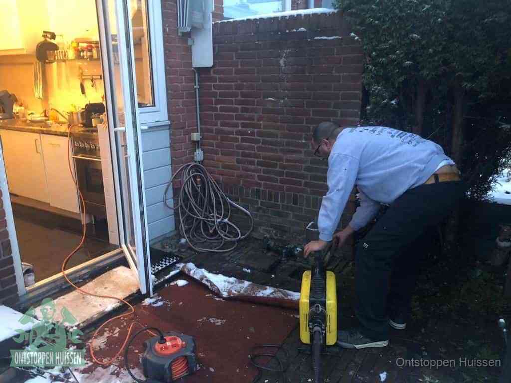 Een monteur werkt buiten bij een open riool-/grondput met een elektrische ontstoppingsmachine om een verborgen afvoerprobleem op te sporen in Huissen