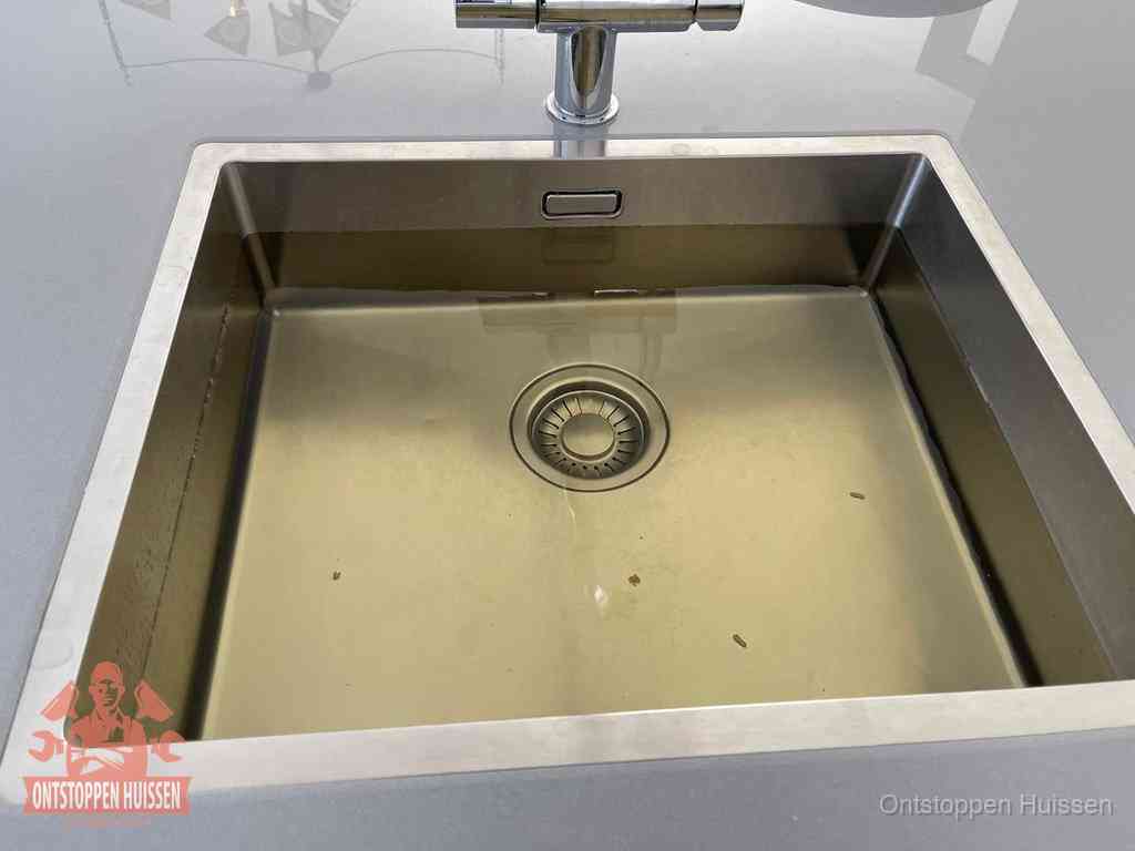 Stilstaand water in een rvs spoelbak dat niet wegloopt, een duidelijk signaal van een gootsteenverstopping in Huissen