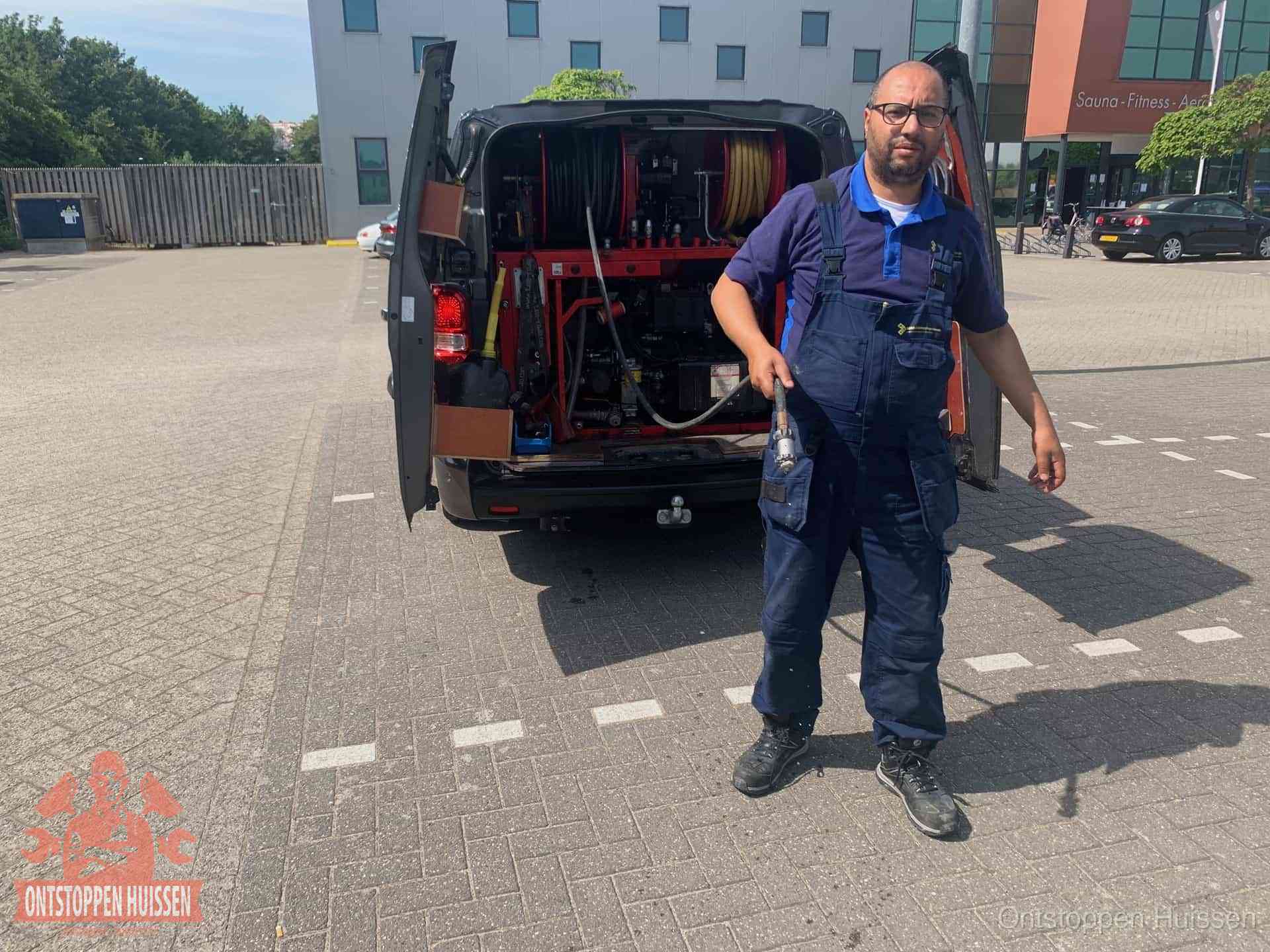 Een monteur bij zijn bestelbus met een hogedruk- en rioolreinigingsunit, klaar om de oorzaak van terugkerende wc-verstoppingen aan te pakken in Huissen