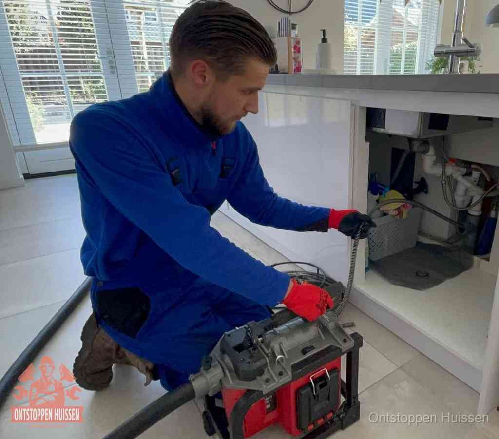 Een monteur voert een ontstoppingsveer in de keukenafvoer onder de spoelbak, waar ook de vaatwasser op aangesloten zit, in Huissen