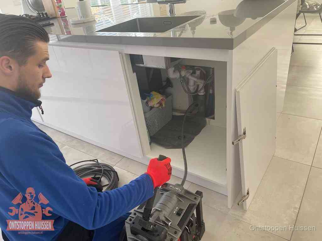 Monteur ontstopt met een veermachine een verstopte afvoer onder de gootsteen in Huissen