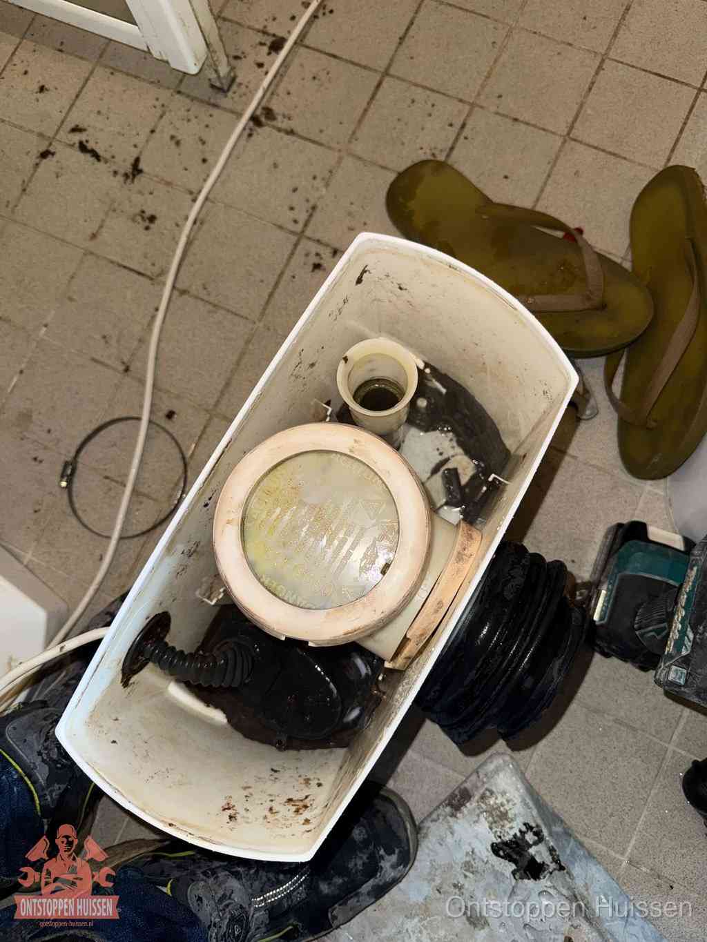 Een gedemonteerde toiletpot op de vloer met ontstoppingsveer en gereedschap ernaast, het verwijderen van een vastzittend voorwerp uit de wc in Huissen