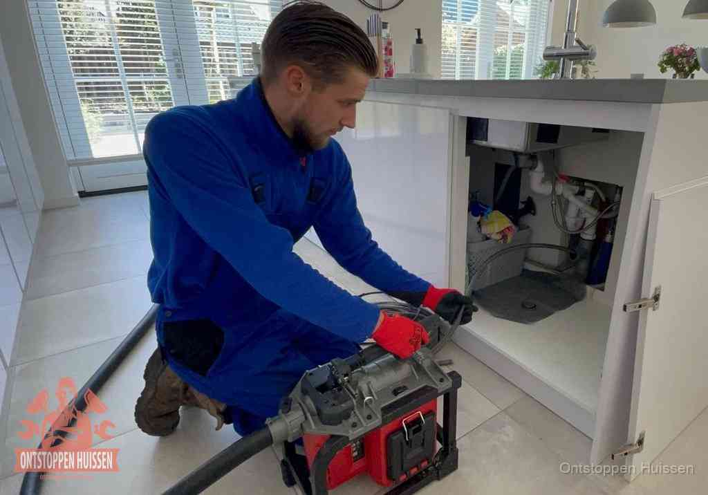 Een monteur voert een professionele elektrische ontstoppingsmachine in de afvoer onder de spoelbak tijdens het gootsteen ontstoppen in Huissen