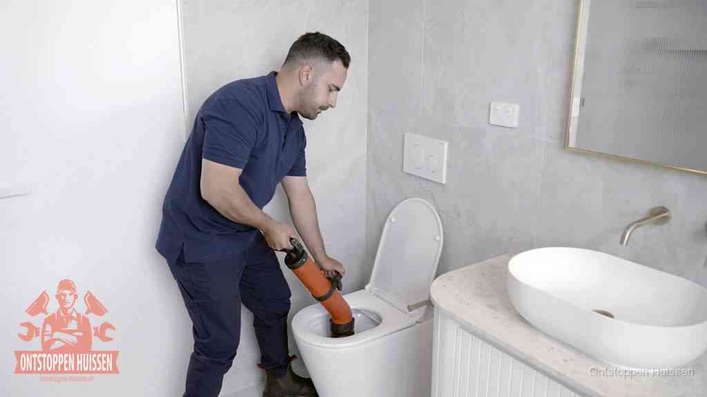 Een man gebruikt een handmatige luchtdruk-ontstopper in een modern betegeld toilet om zelf de wc te ontstoppen in Huissen